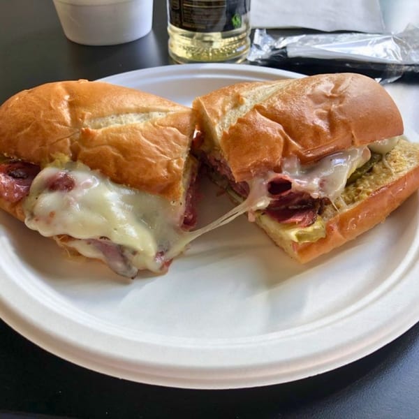 A sliced deli sandwich with melted cheese, meat, and onions on a white plate.