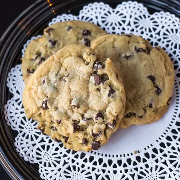 Three chocolate chip cookies on a white doily, served on a dark plate at Rick's DeliCafe.