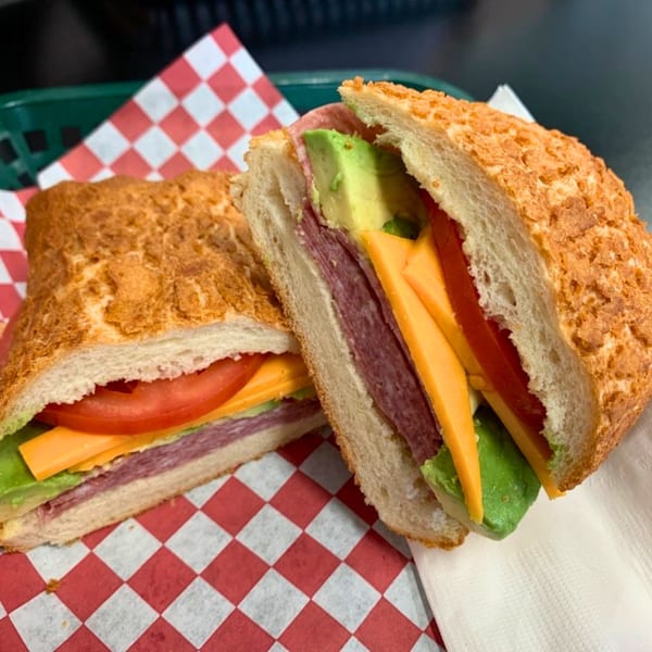 Two halves of a deli sandwich with salami, cheese, avocado, and tomato on a checkered paper.