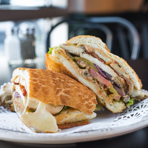 Two halves of a deli sandwich with melted cheese, meat, and vegetables on a white doily.