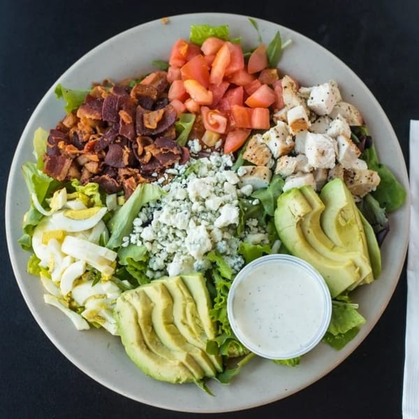 A deli salad with bacon, tomatoes, chicken, blue cheese, avocado, and hard-boiled eggs.