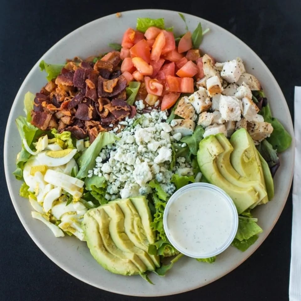 A deli salad with bacon, tomatoes, chicken, blue cheese, avocado, and hard-boiled eggs.